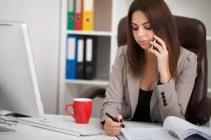 Young business woman working on laptop and talking on mobile phone