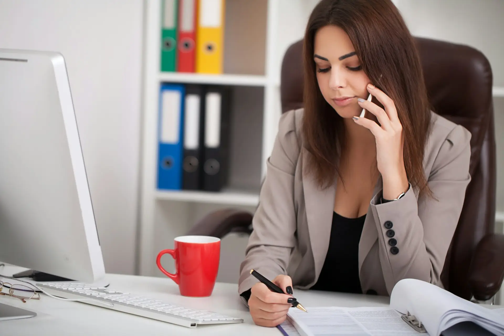 Young business woman working on laptop and talking on mobile phone